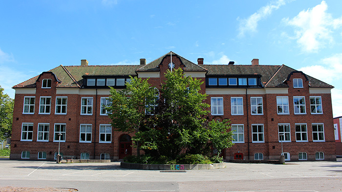 Stort rött tegelhus med stort träd framför.